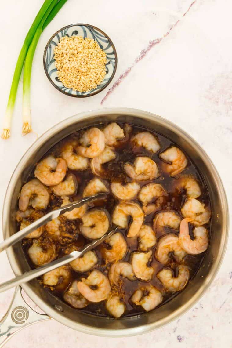 Tongs move shrimp as it cooks in a pan.