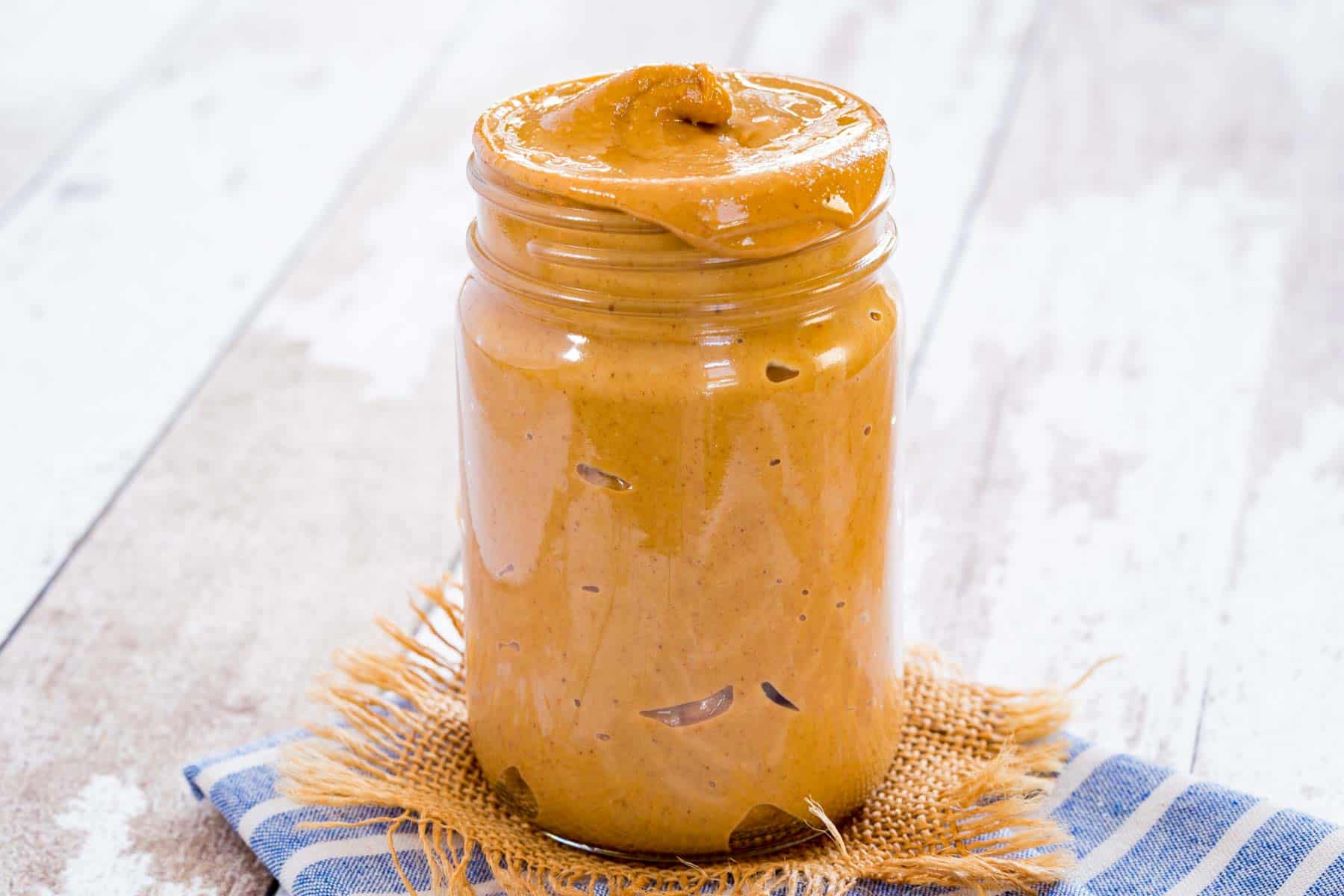 A jar of peanut butter with some dripping over the side.