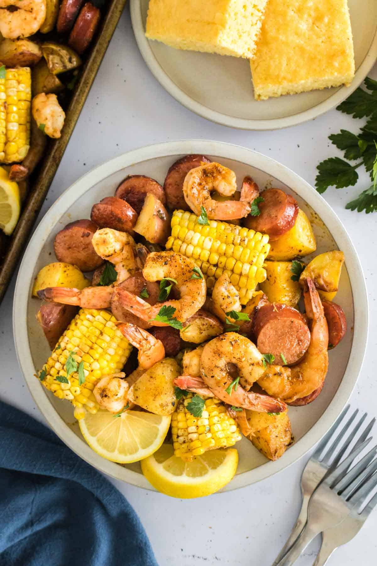 A plate of sheet pan shrimp boil with corn, shrimp, and potatoes in a white boil.