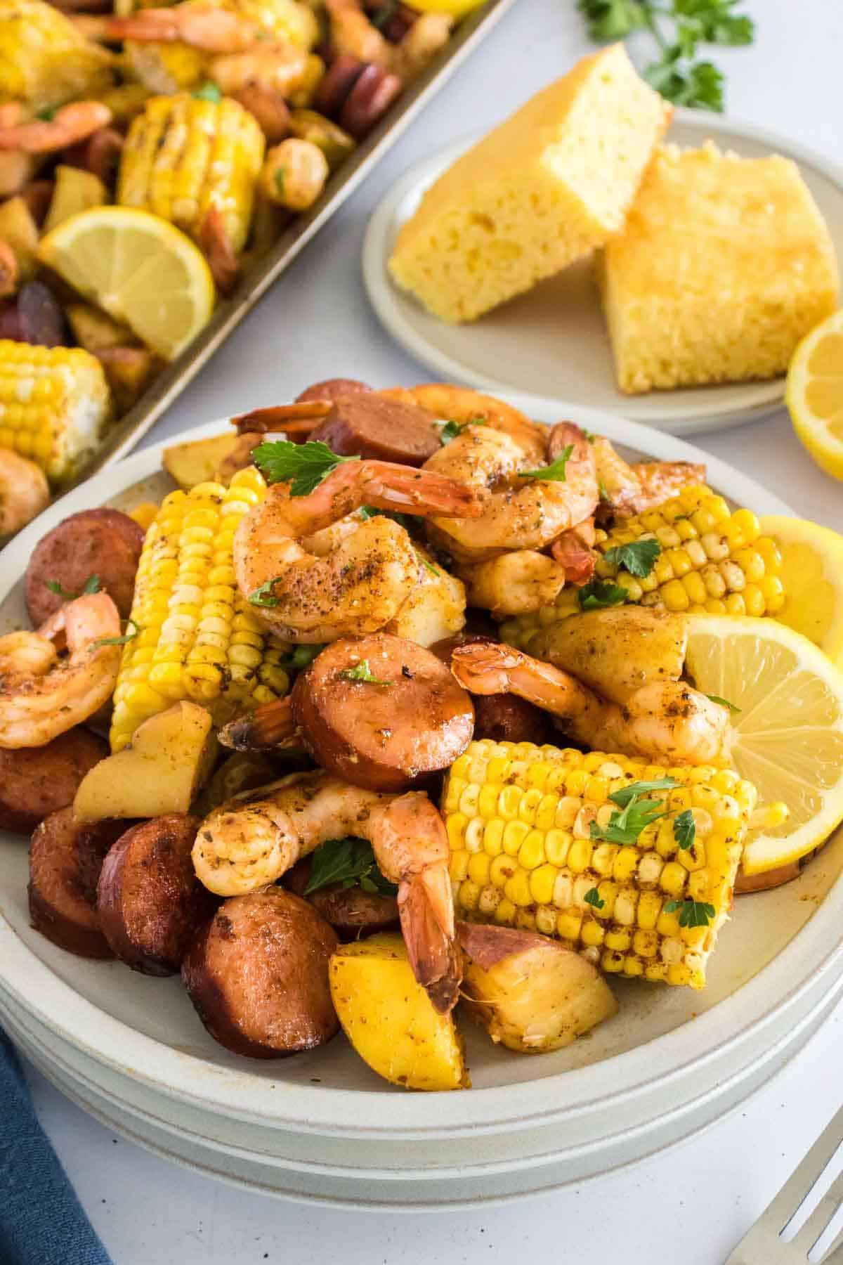 A close-up photo of sheet pan shrimp boil with corn, shrimp, and potatoes in a white boil.