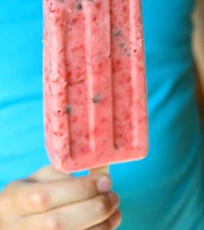 A strawberry popsicle being held by a child's hand.