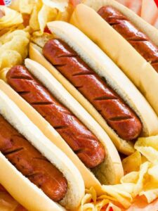Four hot dogs in buns lined up in a basket surrounded by potato chips.