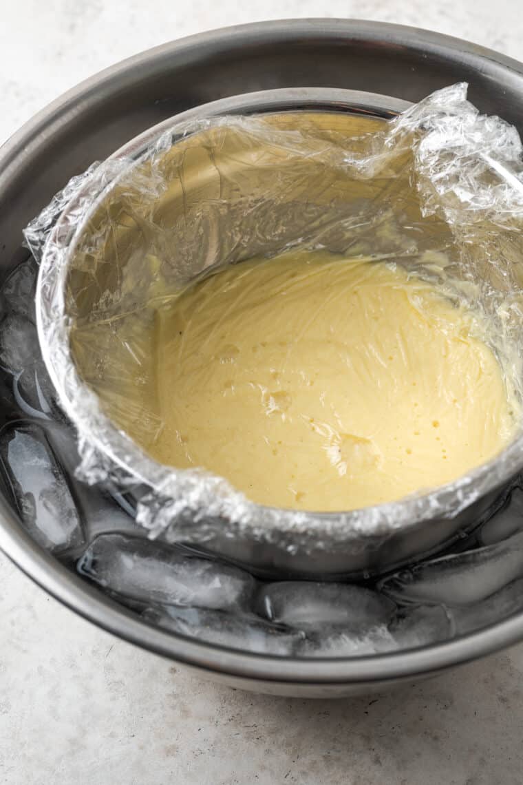 A metal bowl of pastry cream is placed in an ice water bath.