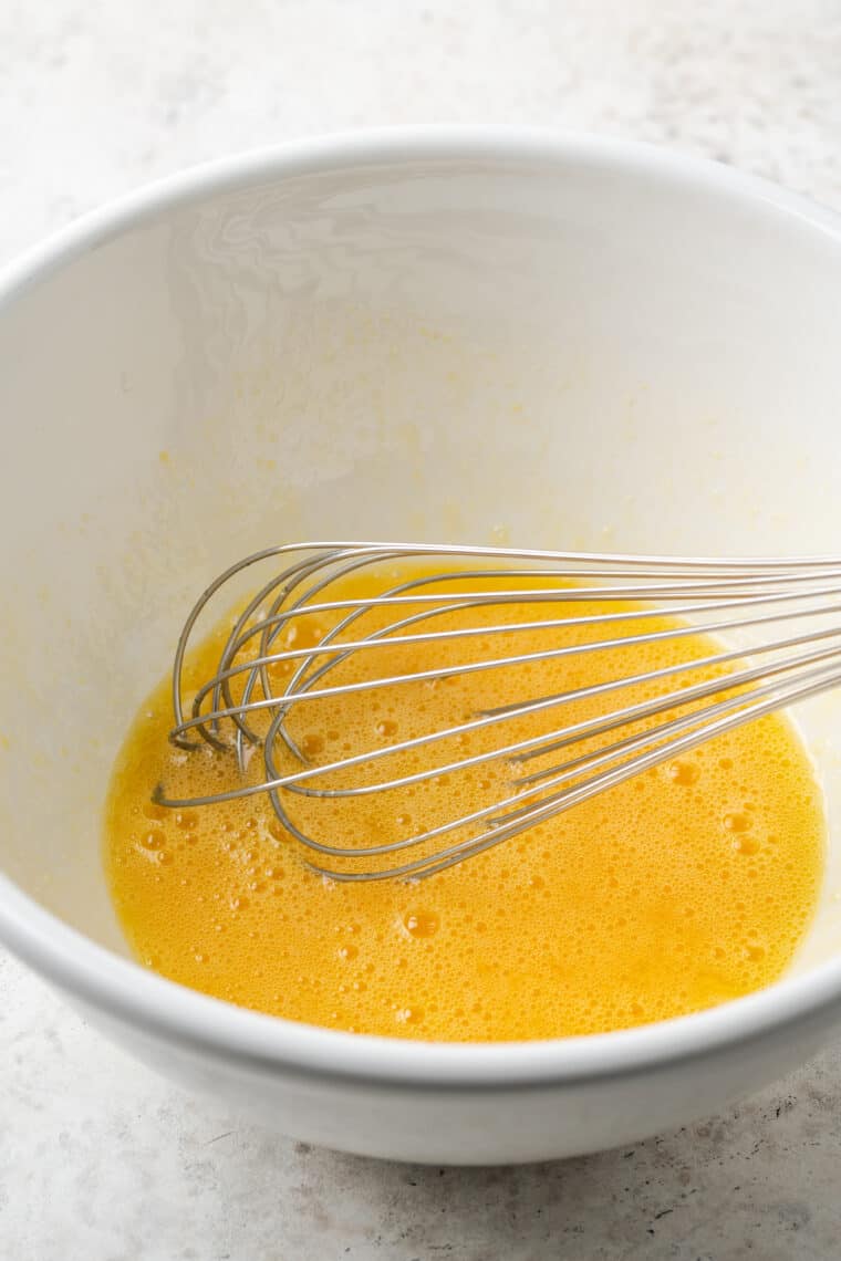 Eggs are whisked in a white bowl.