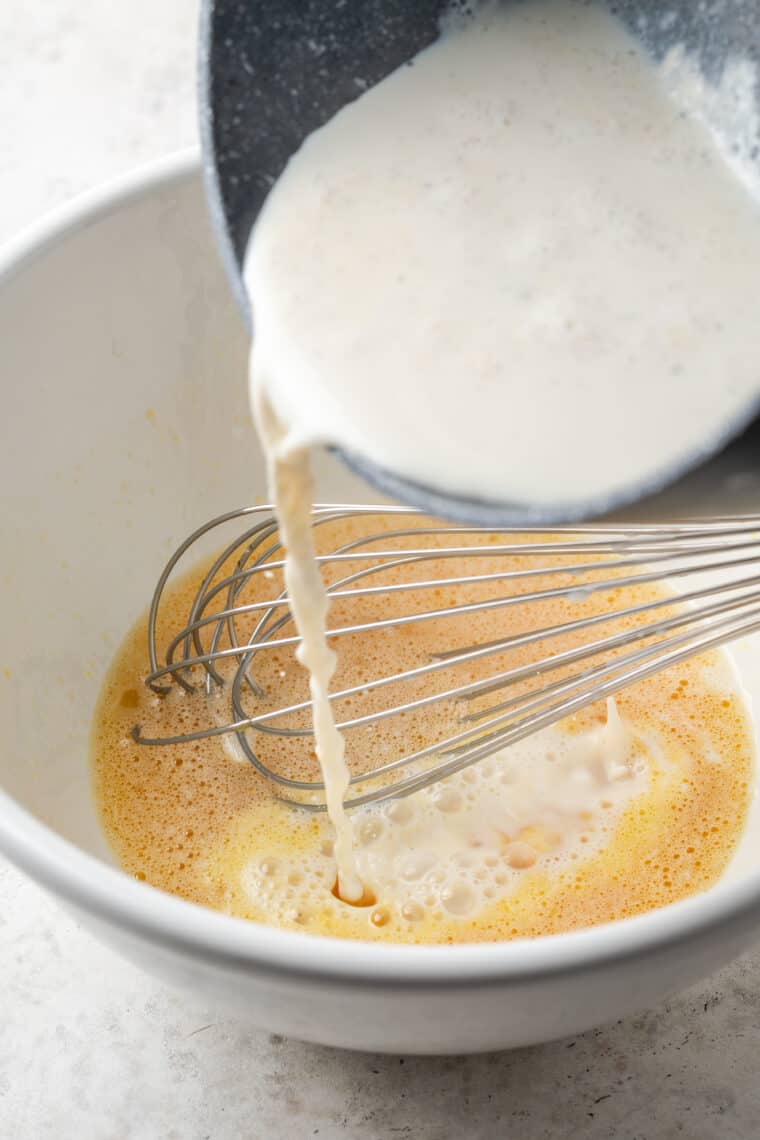 Cream is poured into an egg mixture in a white bowl.