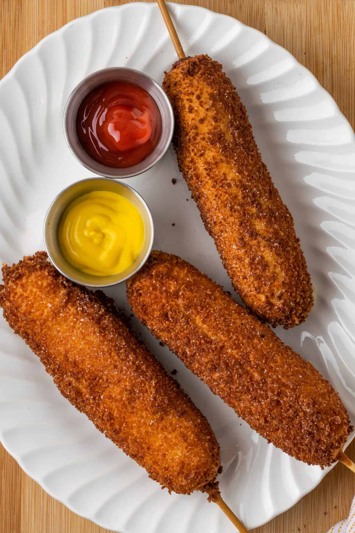 Gluten-free korean corn dogs are shown on a plate with ketchup and mustard.