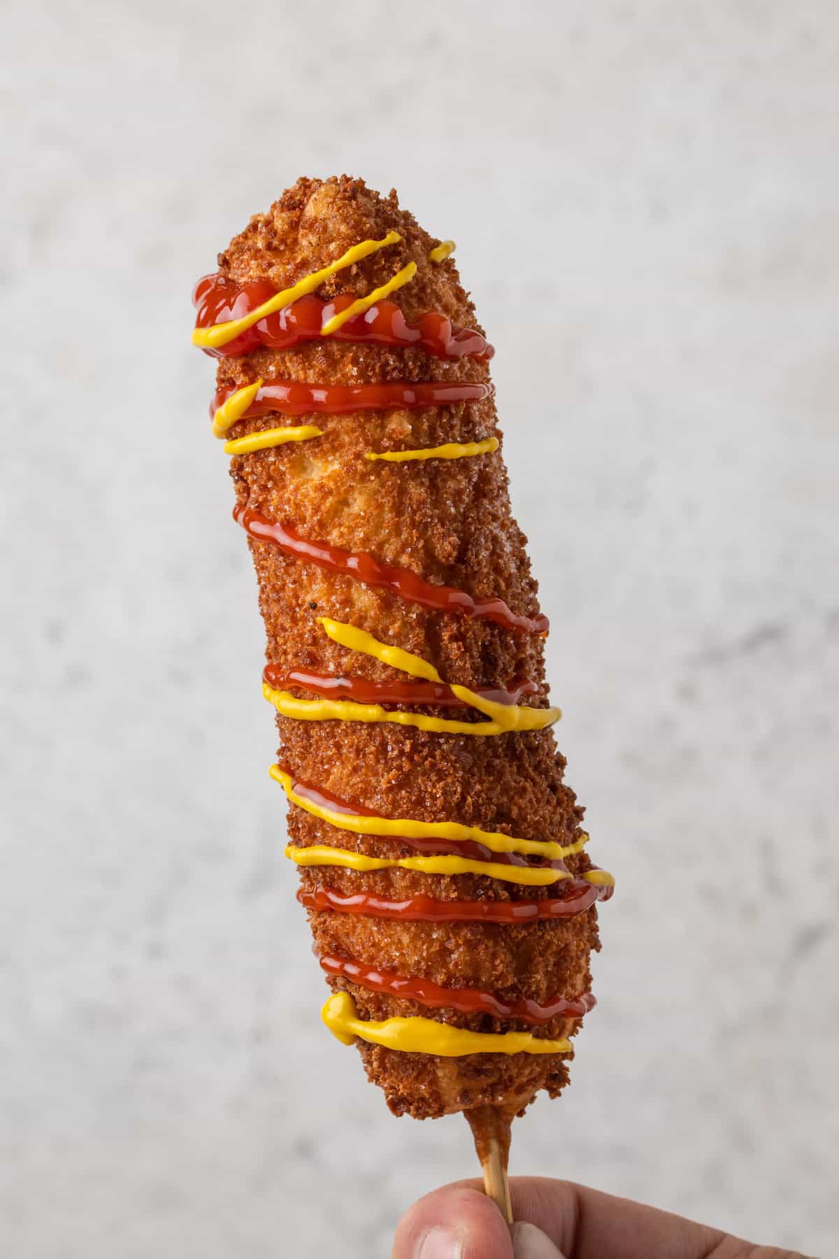 A gluten-free korean corn dog on a skewer and dressed with ketchup and mustard.
