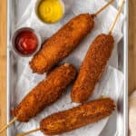 Four gluten-free korean corn dogs are shown on a tray with ketchup and mustard.