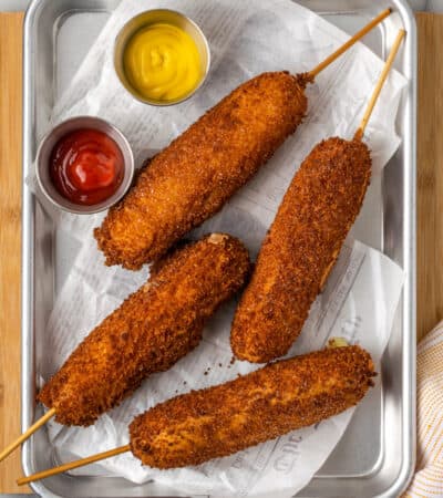 Four gluten-free korean corn dogs are shown on a tray with ketchup and mustard.