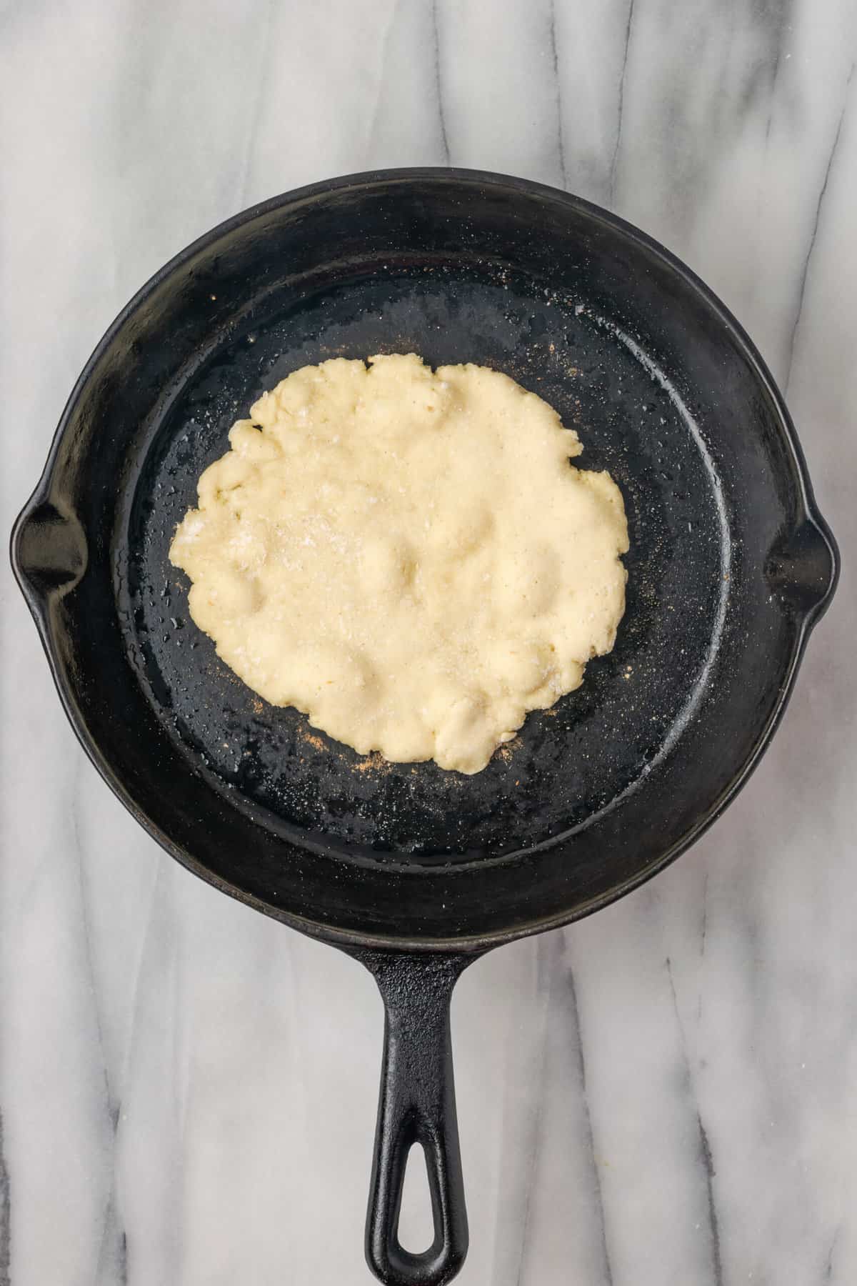 A piece of naan cooks in cast iron skillet.