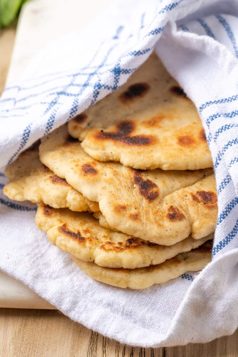 Gluten-free naan bread is wrapped in a blue and white striped towel.