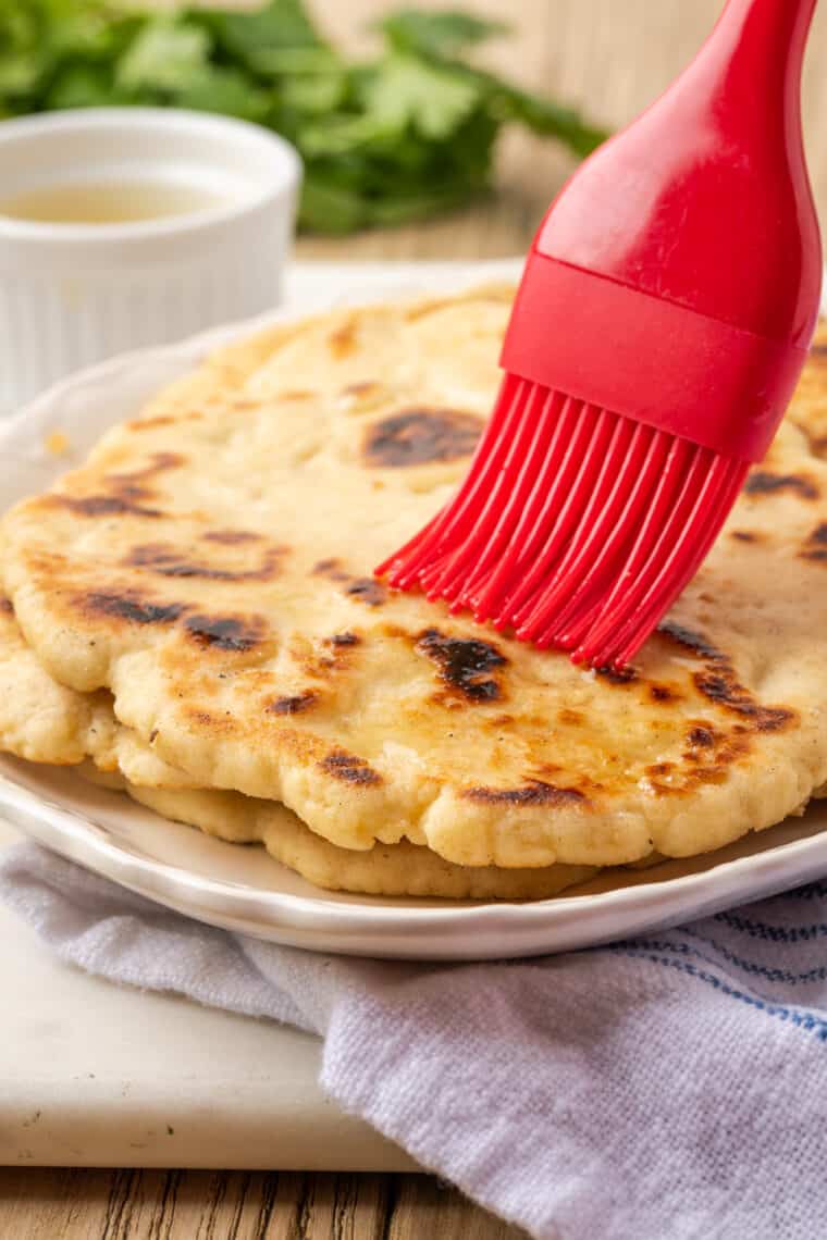 A red pastry brush brushes melted butter on gluten-free naan.