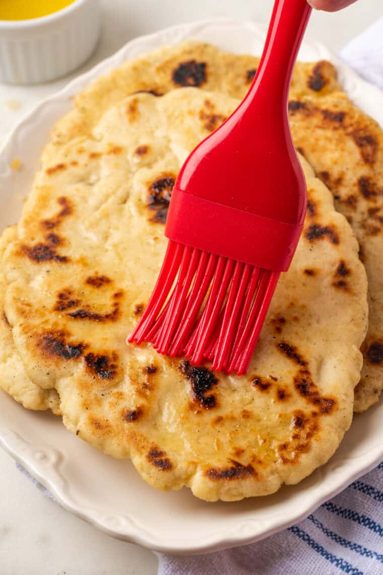 Gluten-Free Naan Bread | Easy Gluten-Free Bread for Wraps and More A red pastry brush brushes melted butter on gluten-free naan.