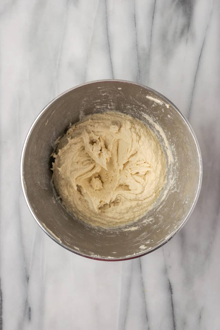 Gluten-free bread dough is mixed in a metal bowl.