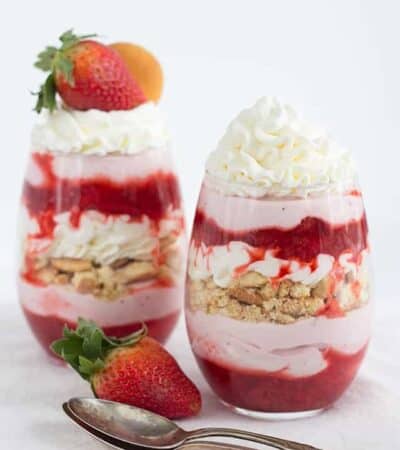 Two strawberry parfaits in glasses with two spoons.