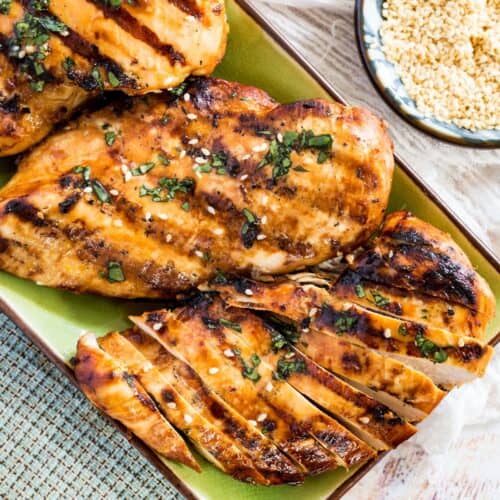 Sliced Asian grilled chicken breasts on a green plate garnished with chopped cilantro and sesame seeds.