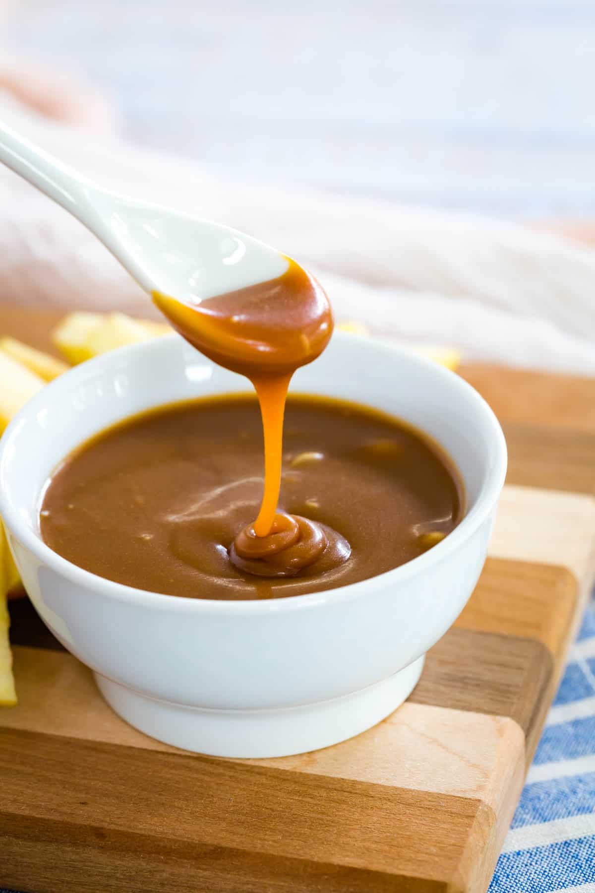 A spoon dips into a bowl of caramel sauce.