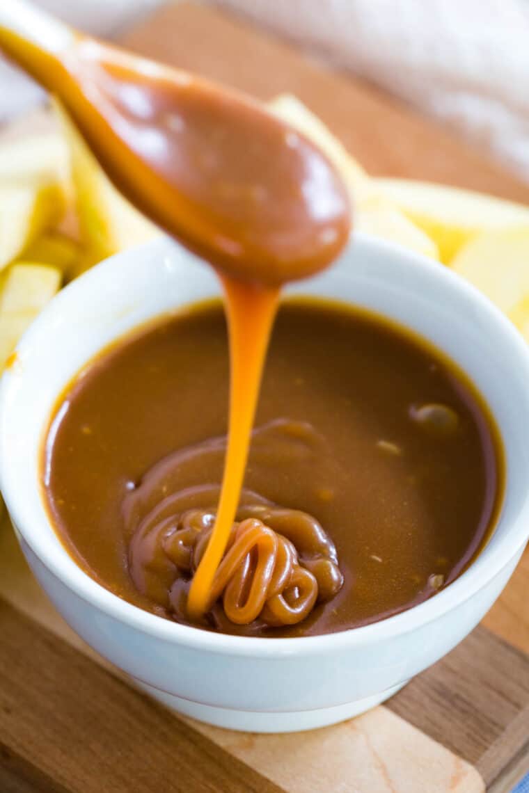 A wooden spoon dips into a bowl of caramel sauce.