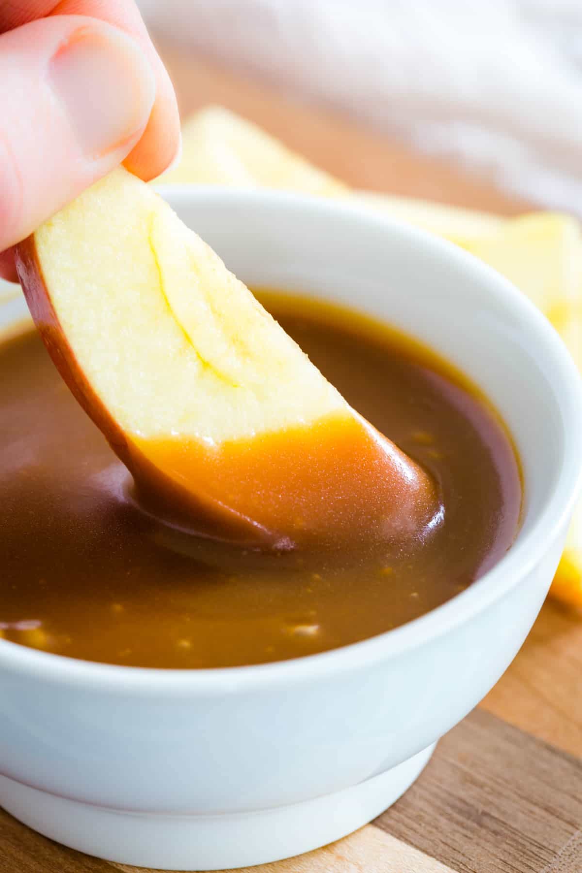 A wooden spoon dips into a bowl of caramel sauce.