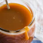 Caramel sauce in a glass jar with a spoon.