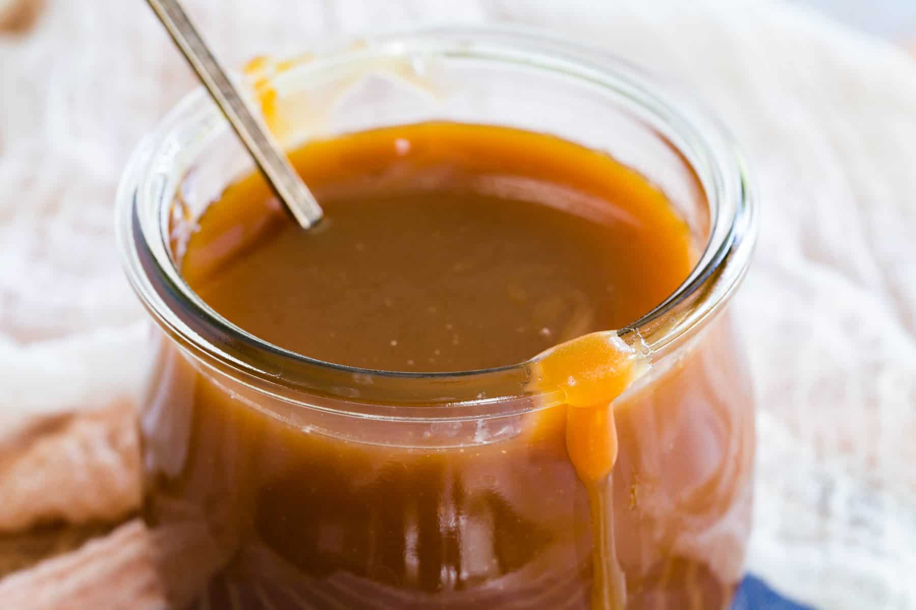 Caramel sauce in a glass jar with a spoon.