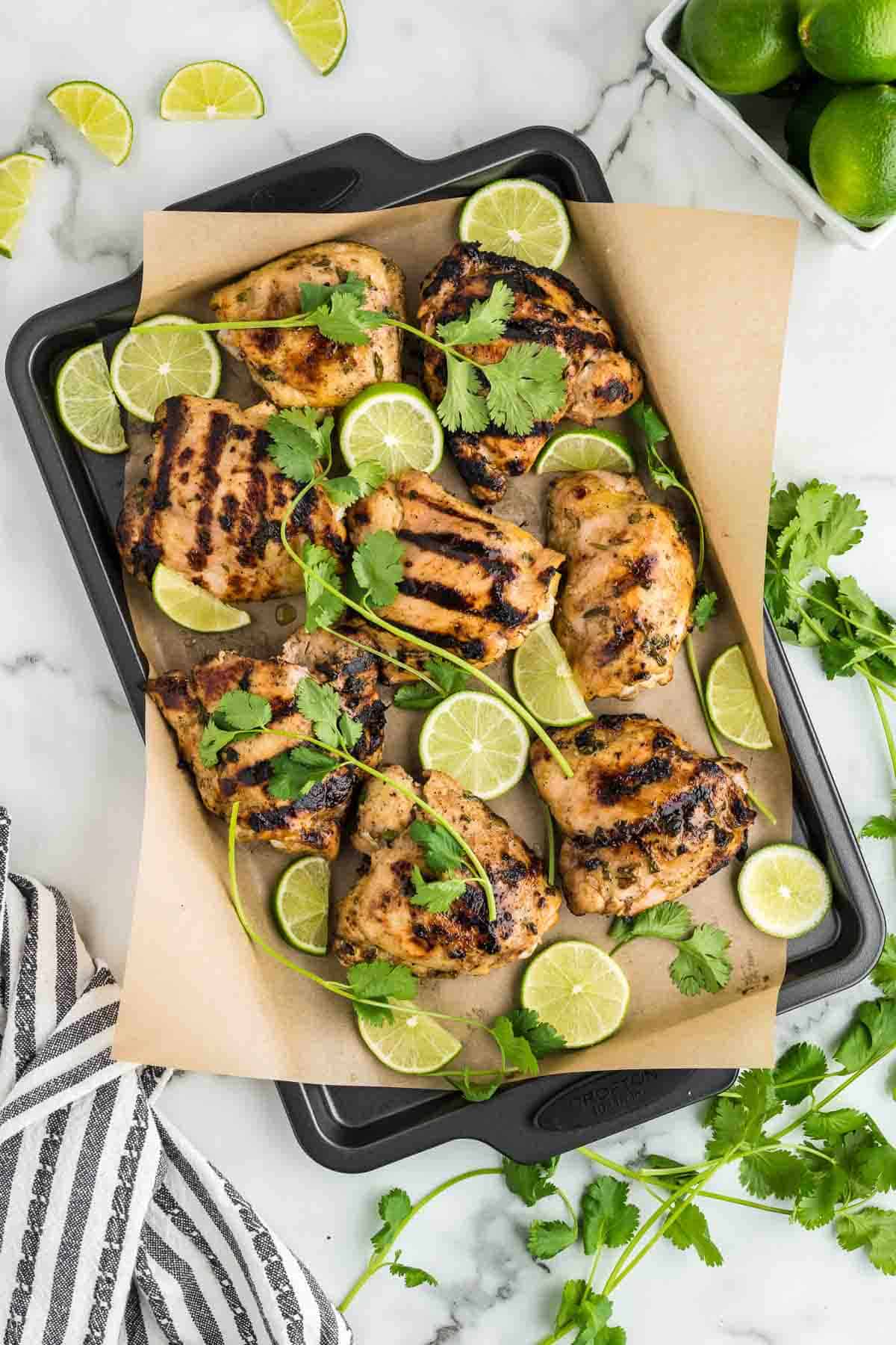 A tray grilled chicken with lime wedges.