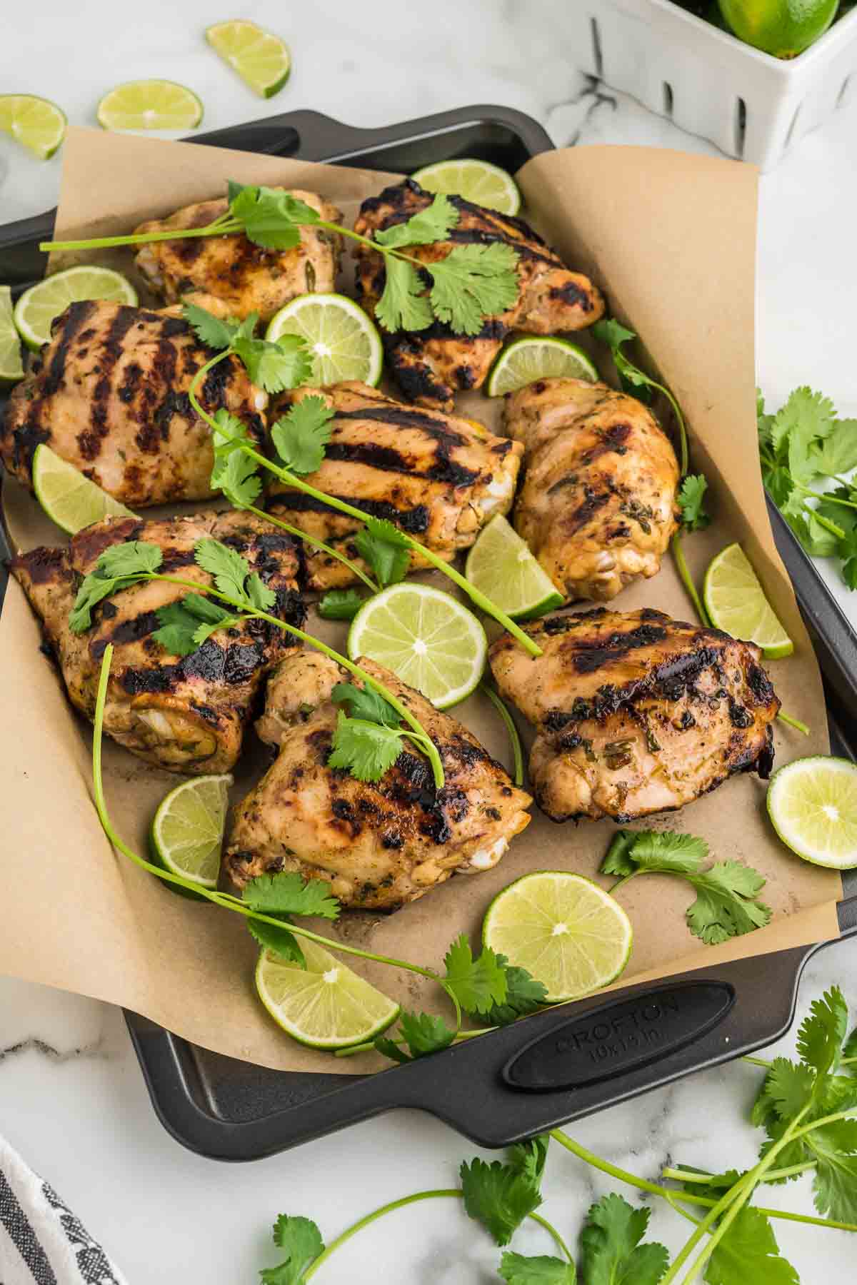 A tray grilled chicken with lime wedges.