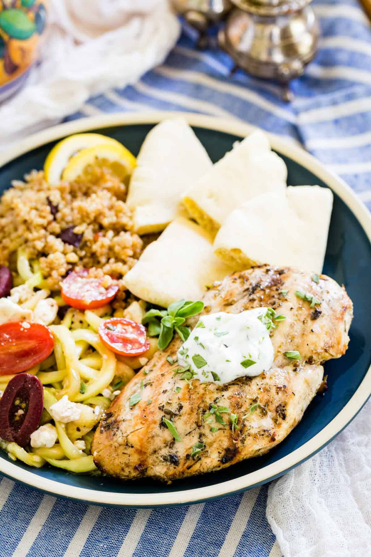 Greek chicken marinade on a plate with vegetables and yogurt sauce.