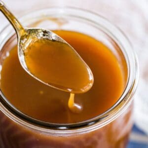A spoon of caramel sauce dripping into a jar of the sauce.
