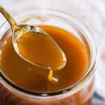 A spoon of caramel sauce dripping into a jar with text overlay that says "Homemade Caramel Sauce".