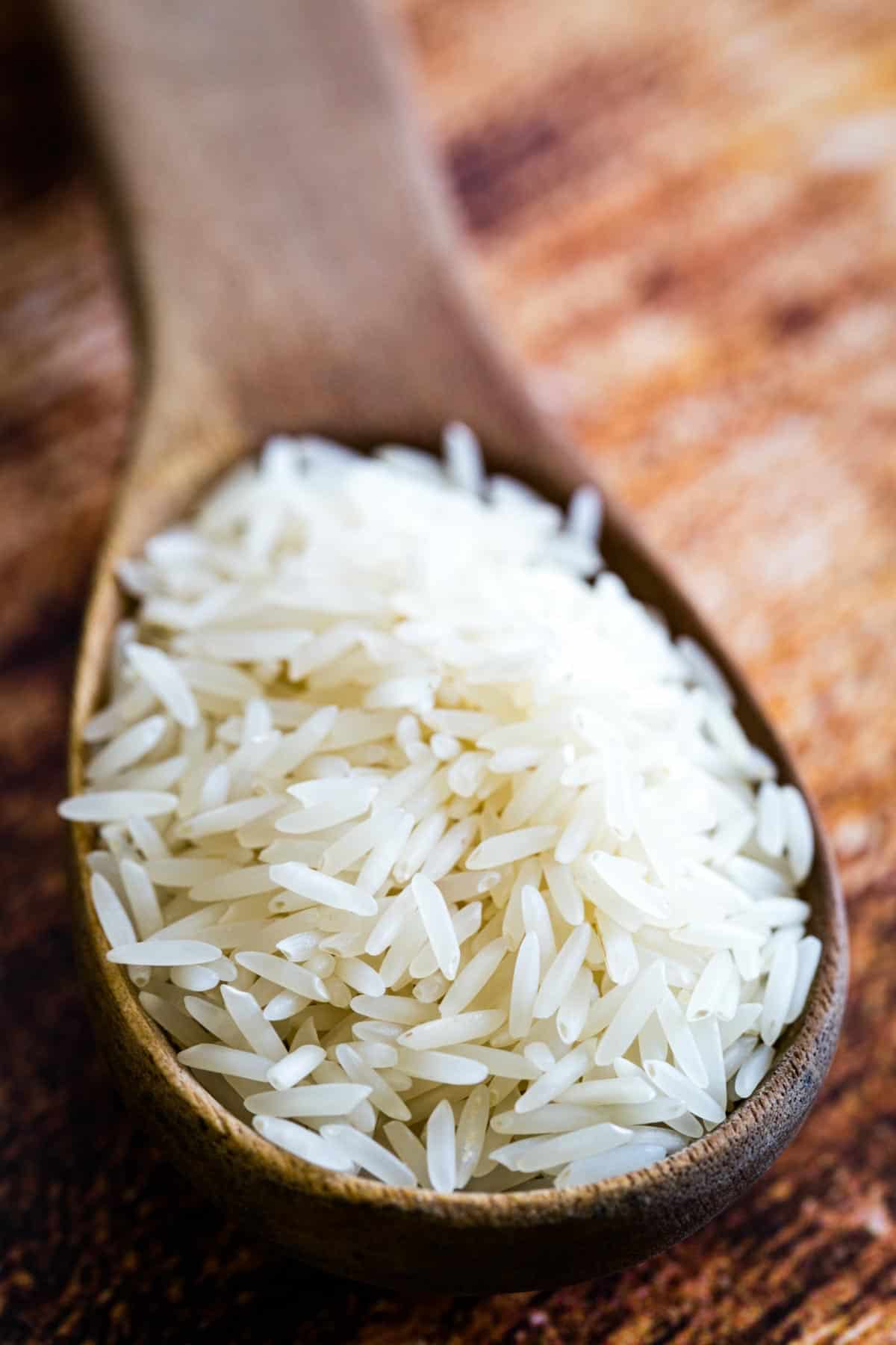 Close up of a large wooden spoonful of basmati rice resting on a wooden countertop.