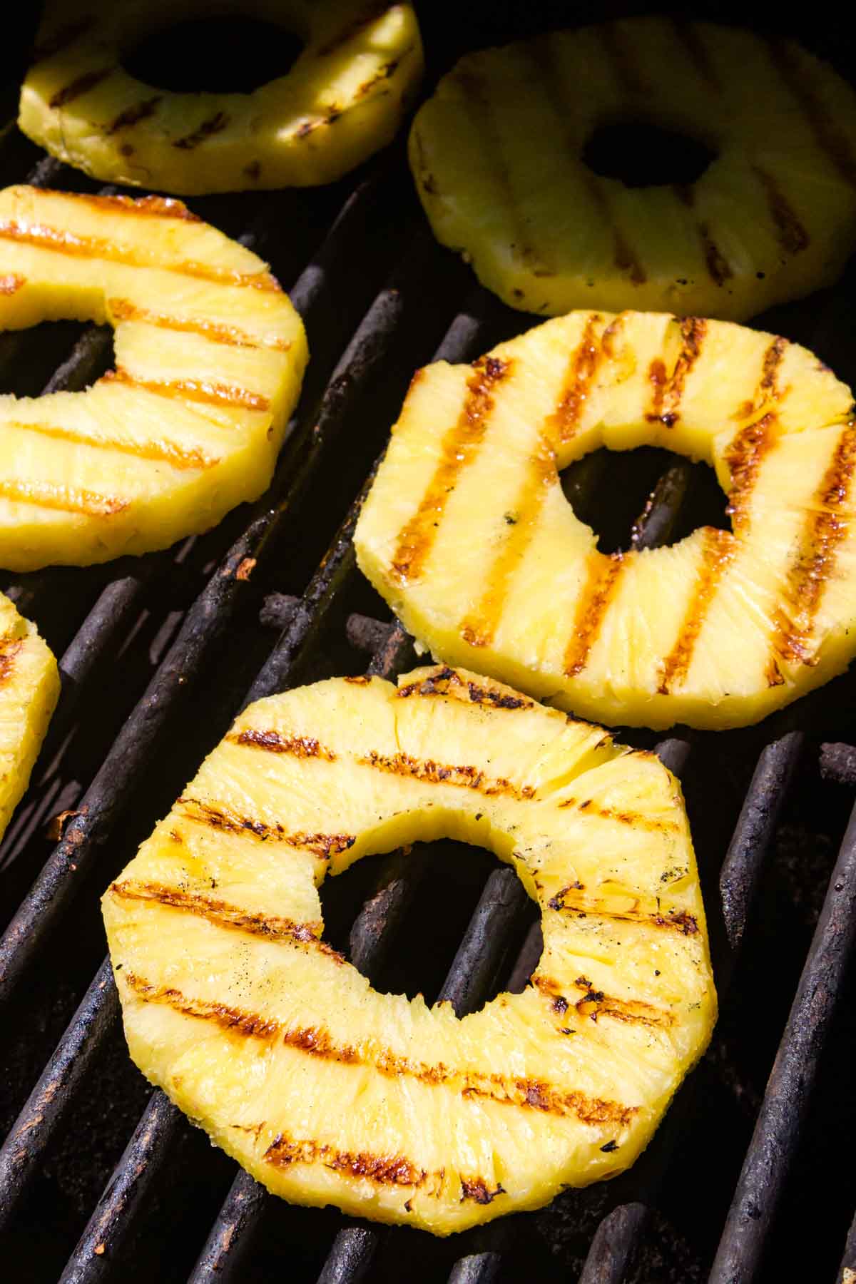 Pineapple slices cook on a grill.
