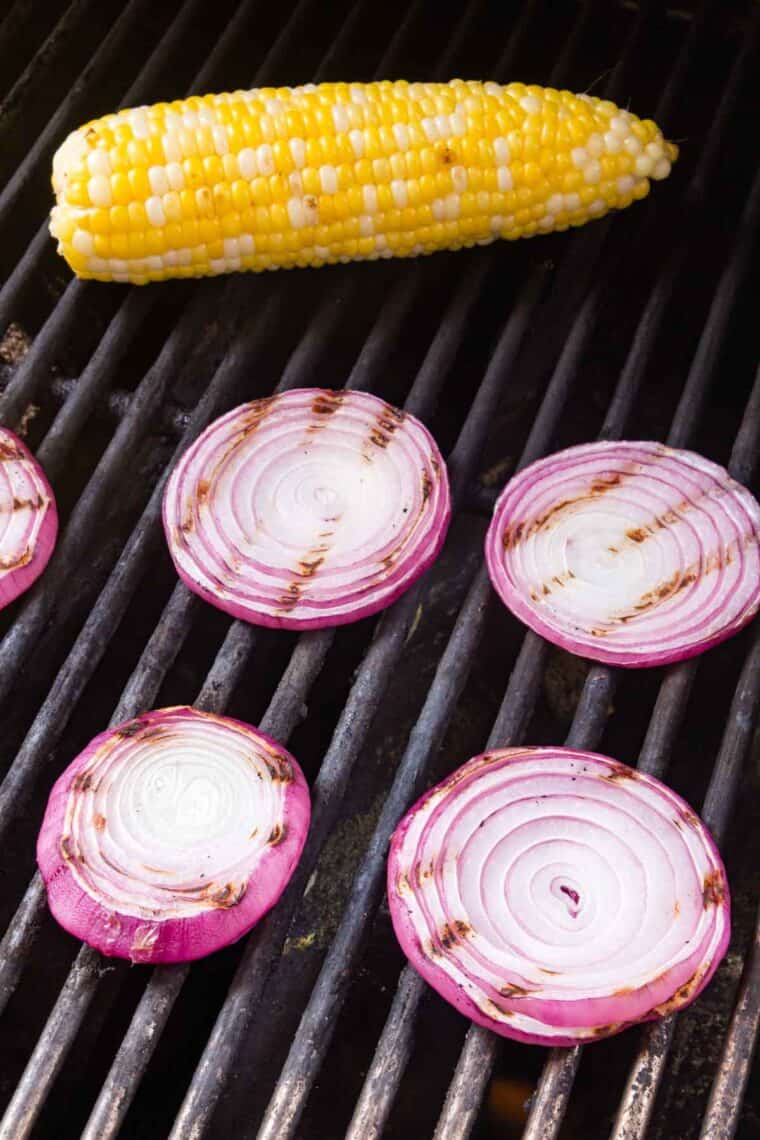 An ear of corn and sliced red onion on a grill.