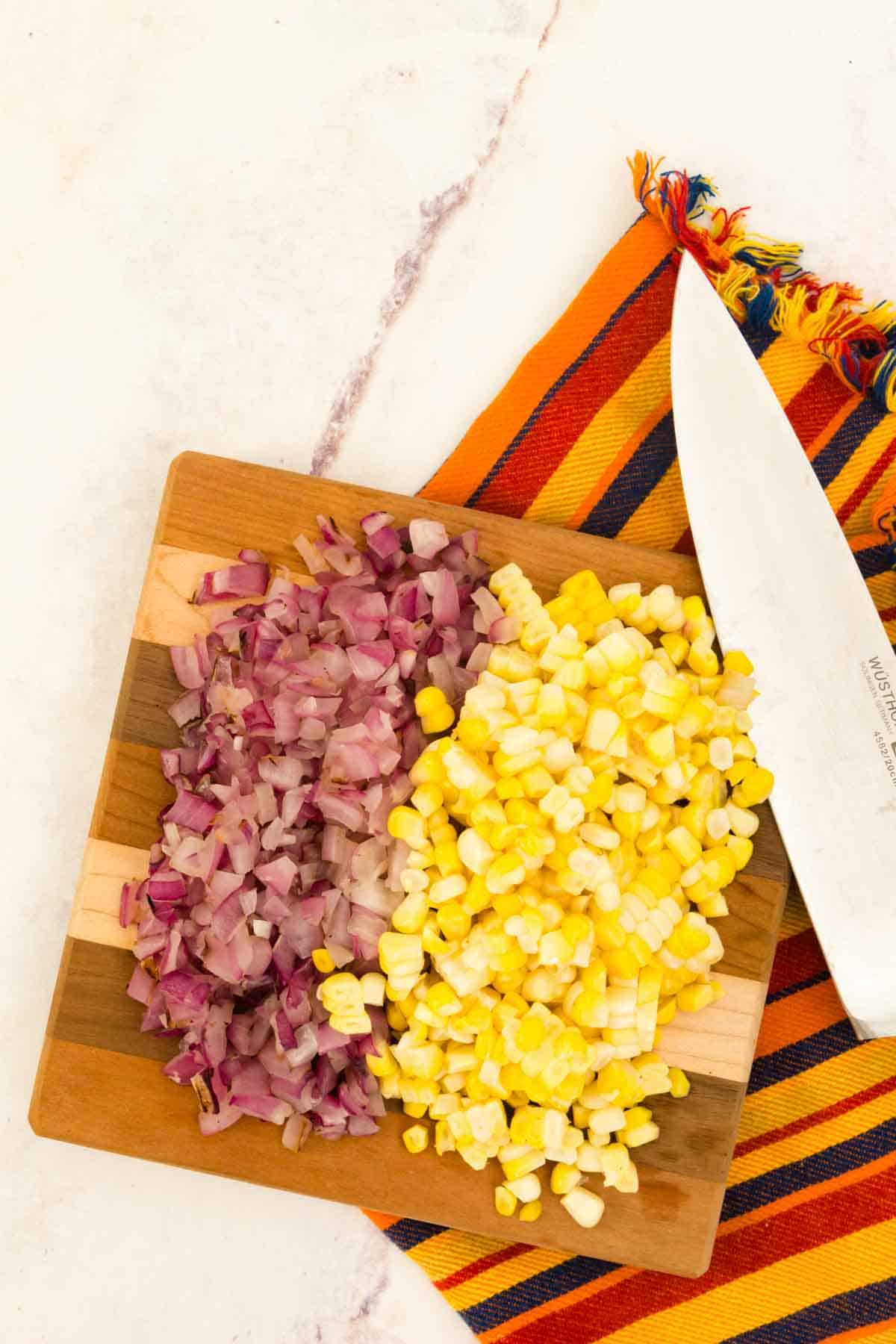 Chopped onions and corn with a knife on a cutting board.