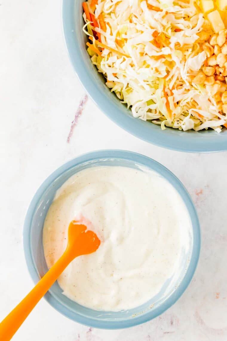Greek yogurt coleslaw dressing in a blue bowl with an orange spatula.