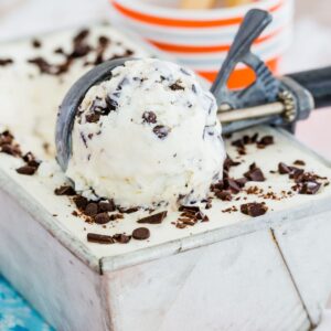 A metal pan of chocolate chip ice cream with an ice cream scoop scooping up some of it.