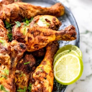 Tandoori chicken legs garnished with cilantro on a platter with lime slices.