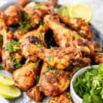 Chicken drumsticks garnished with cilantro on a platter with text overlay that says "Baked or Grilled Tandoori Chicken Legs".