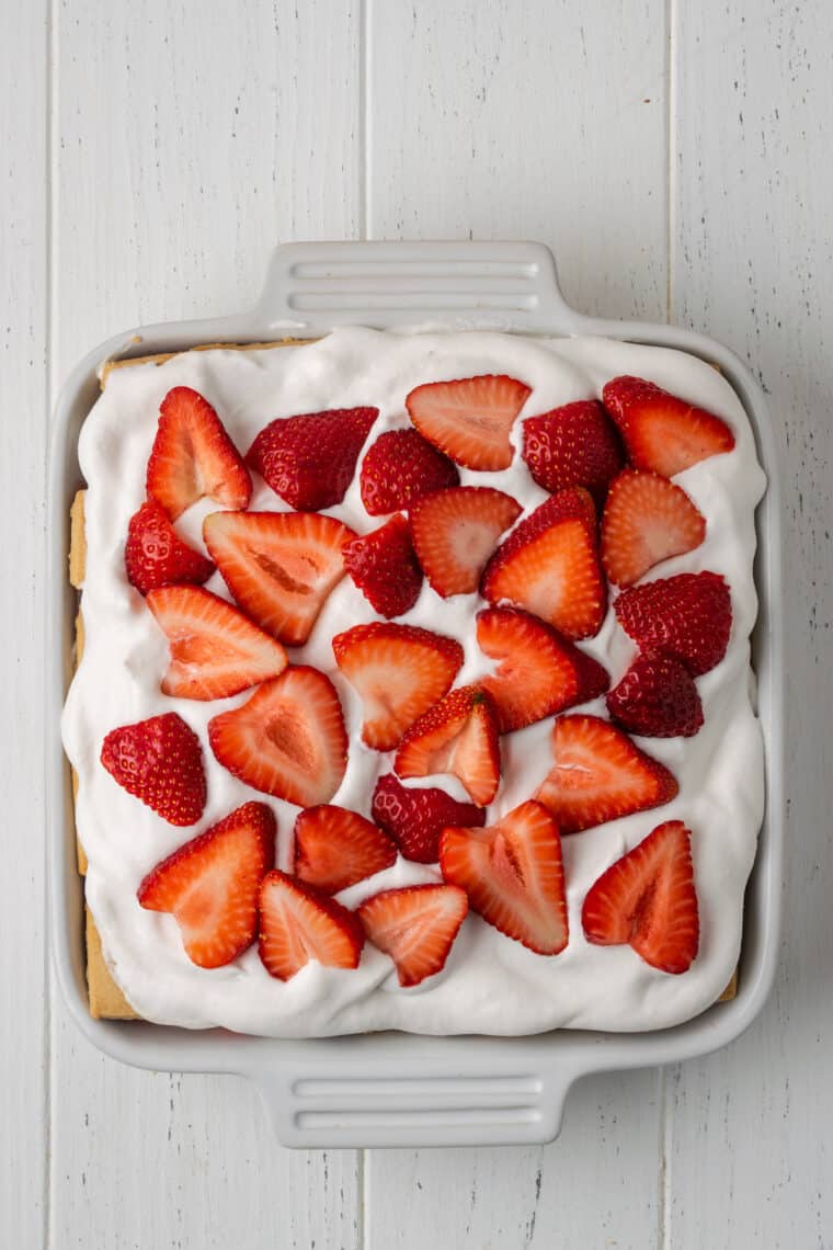 A close up of whipped cream and strawberries on top of icebox cake.