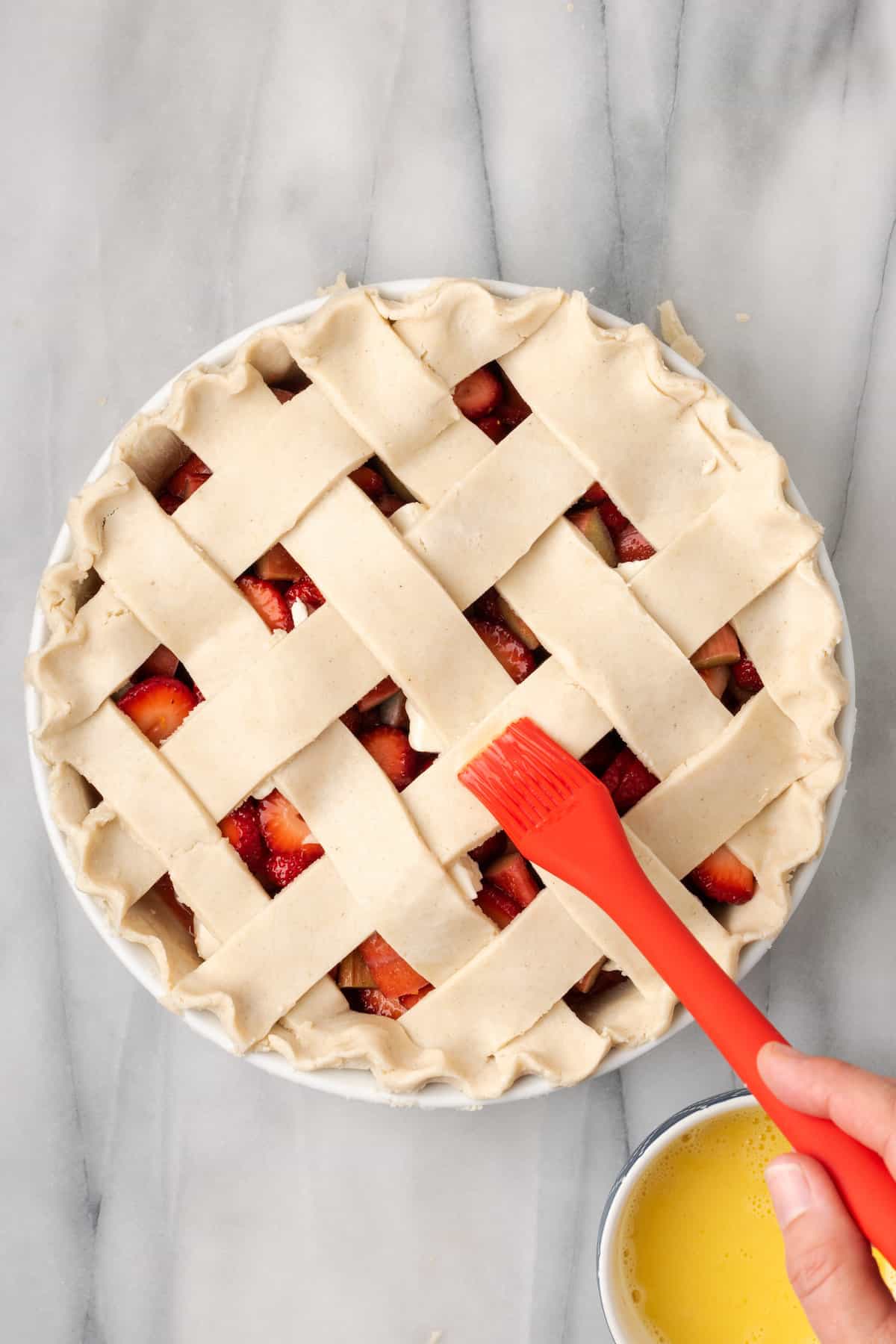 A red pastry brush brushes a pie crust with egg wash.