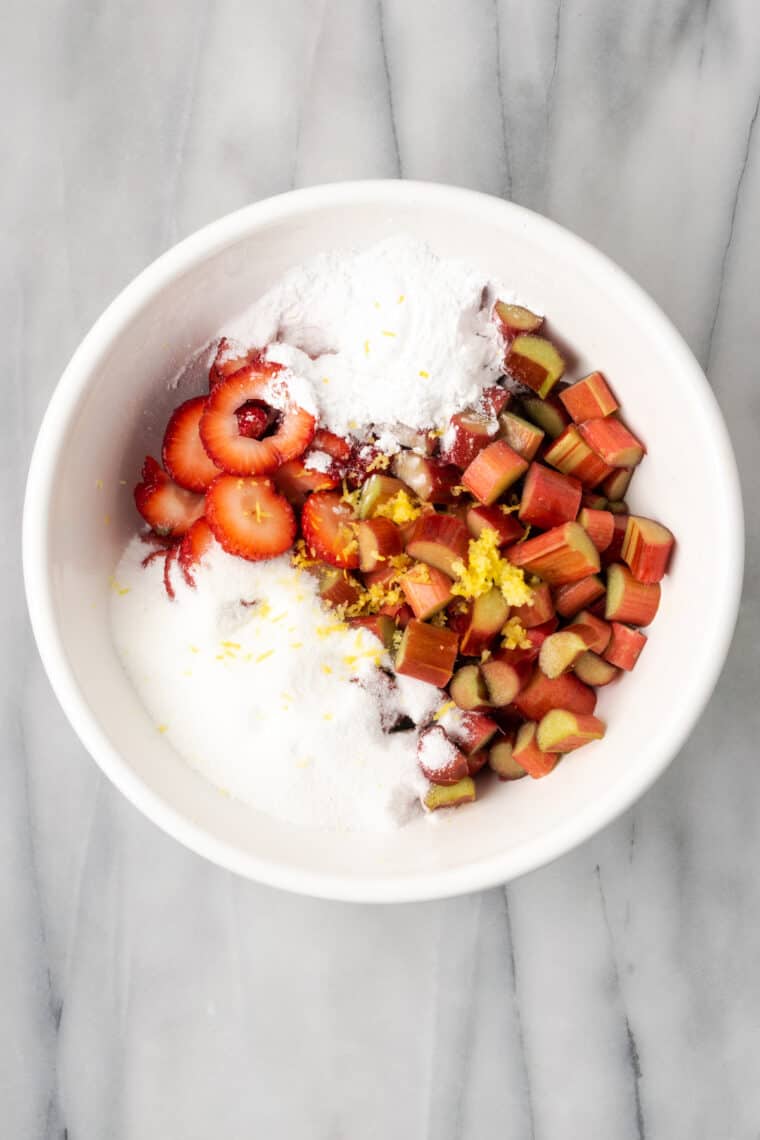 Adding cornstarch and sugar to a bowl of strawberries and rhubarb.