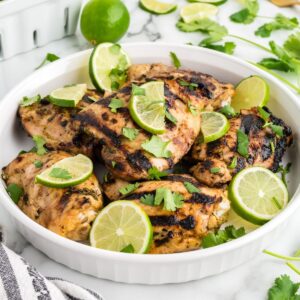 A dish of grilled chicken thighs garnished with minced cilantro and lime slices.