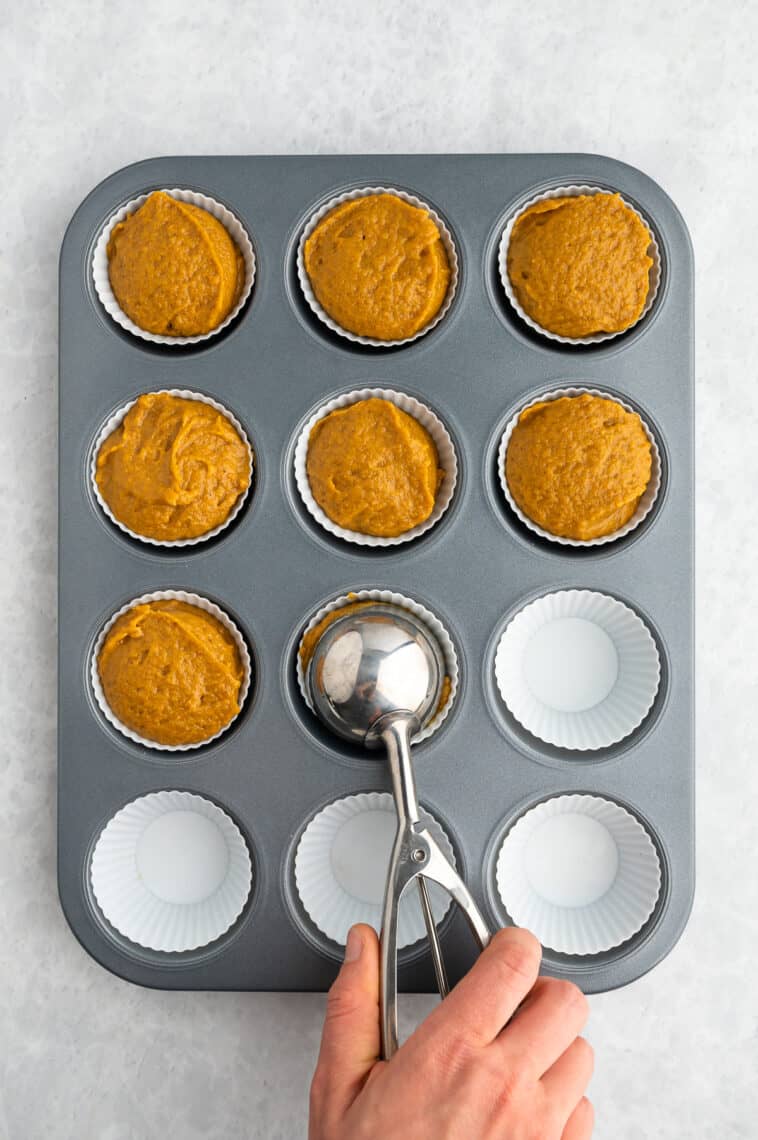 A muffin scoop fills a muffin tin with batter.