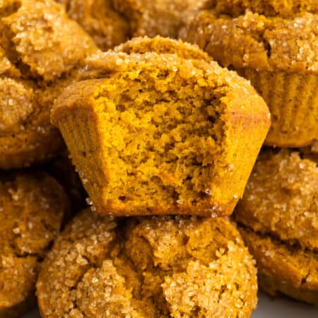 Gluten-free pumpkin muffins on a plate, one has a bite taken out from it.
