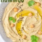 A bowl of hummus garnished with olive oil, chickpeas, sesame seeds and fresh cilantro with text overlay that says "Classic Hummus".