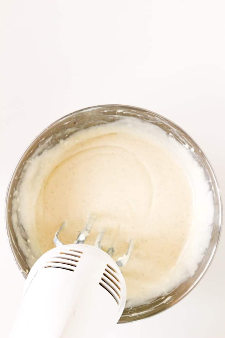 A hand mixer blending the cream cheese and sweetened condensed milk mixture.