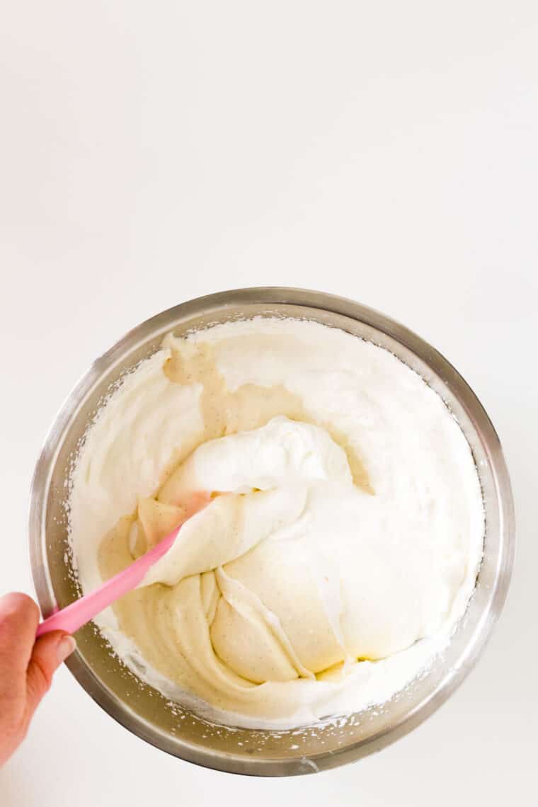The cream cheese and sweetened condensed milk mixture being folded into whipped cream with a pink spatula.
