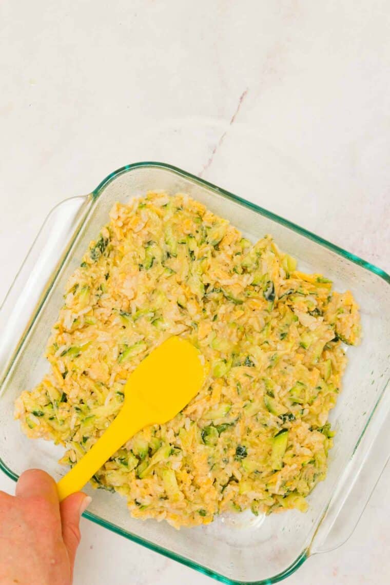 Casserole mixture being spread in a glass baking pan with a spatula.