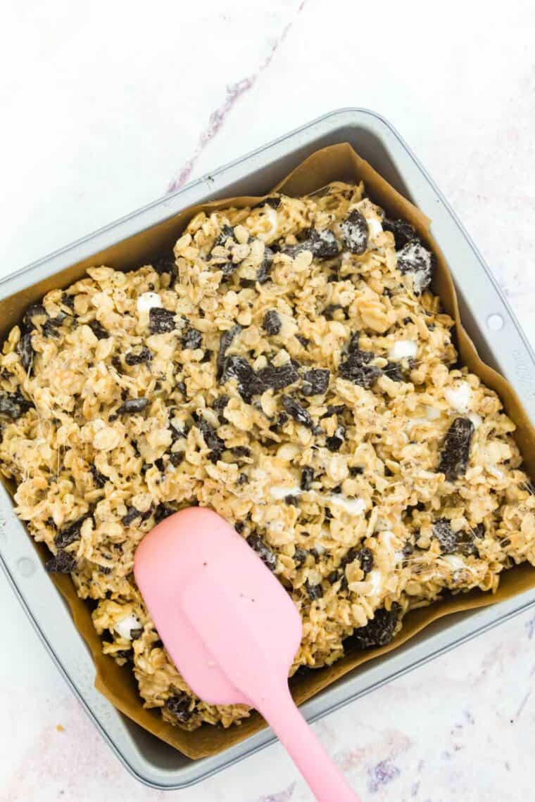 A pink spatula spreads rice krispies treats in a pan.