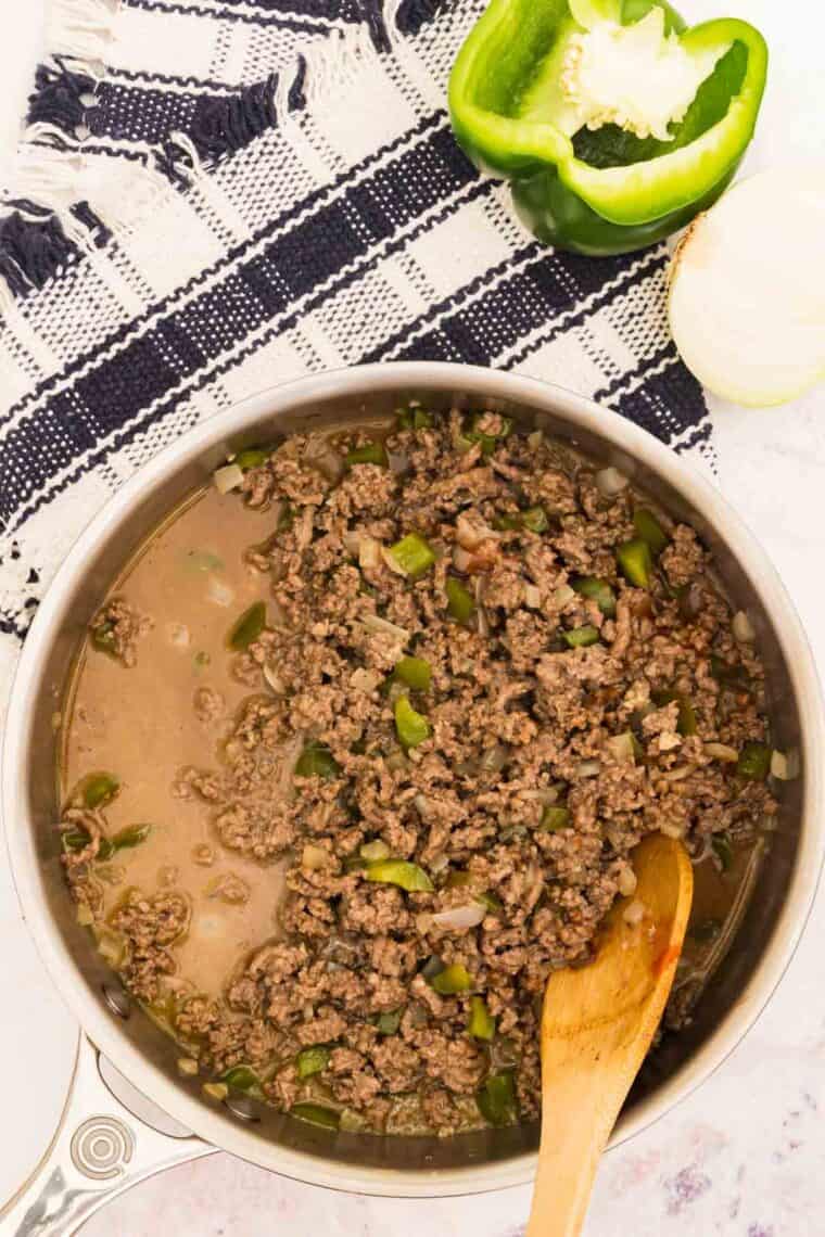 Cooking sloppy joes filling in a pan with a wooden spoon.